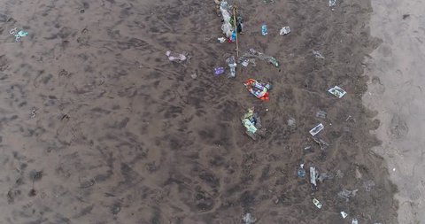 Drone footage of plastic waste washed ashore on the beach in Seminyak, Bali. The camera is facing down at the trash on the sand and is going along the beach.