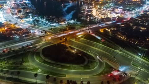 Aerial time lapse in motion or hyper lapse at night over a traffic circle onramp and up street showing streaks of car lights, city buildings and parking lots, showing the fast paced city lifestyle.
