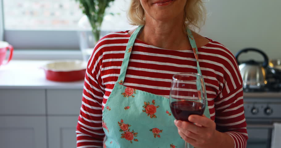 Portrait of smiling Caucasian woman showing a glass of red wine in kitchen at home