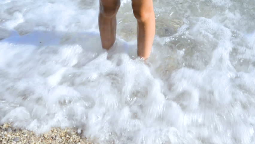 The legs of children playing in the sea. Standing on pebble beach and waiting for waves. Concept for summer beach vacation