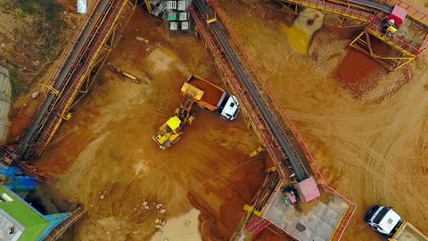 Excavator loader loading sand into dumper truck. Aerial view of excavator loader working on sandpit. Backhoe excavator loading sand in dumper truck