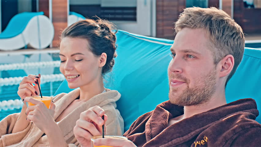Young couple drinking cocktails on deckchairs near pool. Shot in Red Epic Dragon