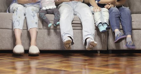 A cheerful family is sitting on the couch and playing with their feet. 4K footage.
