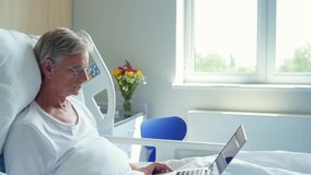 Senior man lying in the hospital bed with laptop