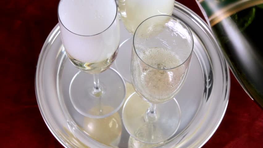 bottles comes into frame and pours champagne into flutes on silver tray