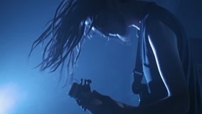 Guitarist rocker with dreadlocks playing the electric guitar on stage. Performance music video rock, punk, heavy metal band in slow motion.