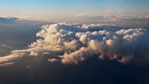 Flying over the evening clouds with the late sun. Flight through moving cloudscape with beautiful sun rays. Traveling by air through an airplane window. Perfect for cinema, background