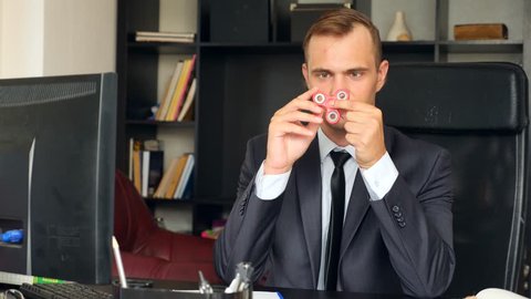 Red hand spinner, rotating on man's hand. Man in a suit spinning a fidget spinner in his office at his desk. Twists on the nose. 4k. Slow motion