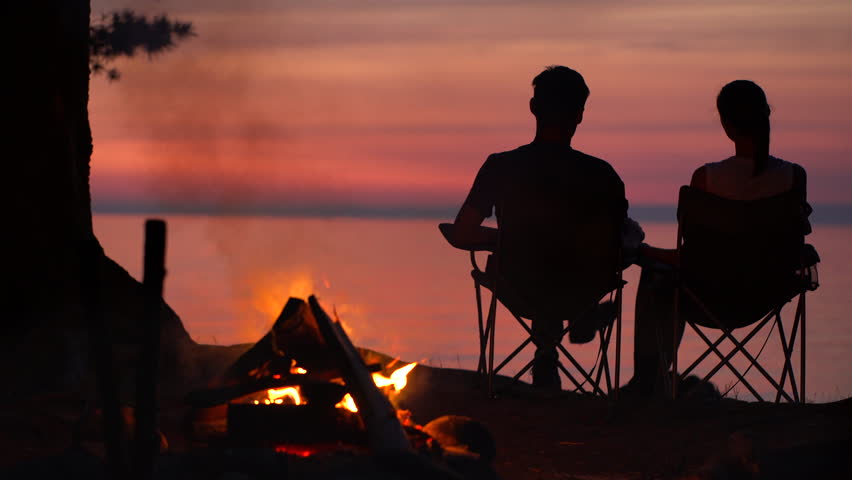 Couple is Sitting near Campfire at Night And Looking at brilliant red sunset at the sea | Shutterstock HD Video #29645443