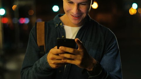 Attractive man in the denim shirt using smart phone in the street at the evening time in the city.