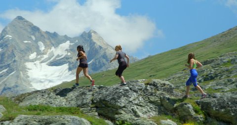 Three very different women run up and over a mountain ridge with peaks and glaciers.