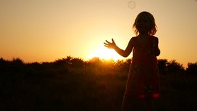 The child is played with soap bubbles. Video in slow motion on a sunset background.