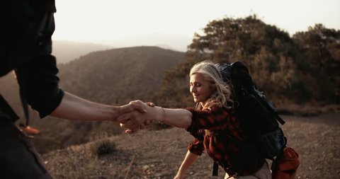 Mature woman on a hikinig adventure holding man's hand helping her climb on mountain hill