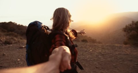 Senior woman hiker holding husband's hand and reaching mountain peak with panoramic view at sunset