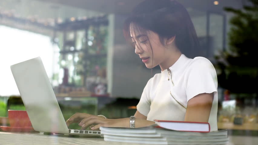 Young Asian Teenage girl having a relaxing time in a coffee shop working and chatting on a computer laptop on a bright sunny day Royalty-Free Stock Footage #29678995