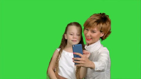 Cute family mother with child daughter taking selfie smart phone photo on a Green Screen, Chroma Key