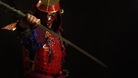 A samurai man in a beautiful red armor and a red defensive mask of a demon pulls the katana out of the sheath and holds it in his hands