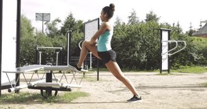 Side view of woman in sportive clothing listening to music and stretching legs while working out in street gym in park looking forward.