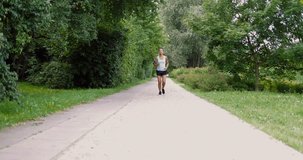 Young ethnic cheerful woman in sportswear listening to music with smartphone and running in summer park smiling at camera.