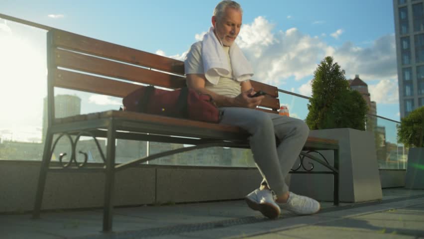 Joyful sporty aged man resting on the bench