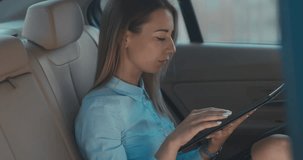 Attractive elegant business lady executive rides in a car with brown leather seats, using her portable tablet computer. 4K UHD RAW edited footage
