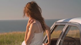 Back view of young brunette woman traveller enjoying sunset standing outside car