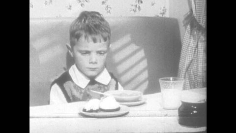 1950s: Grumpy boy at meal table. Boy makes angry face without speaking. Woman talks and looks annoyed. Woman picks up room and talks angrily.