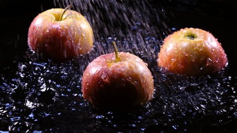 Amazing shower for three pink apples in back light close up. Yummy fresh fruit on black background with excellent texture in slow motion, 240fps. Vibrant eco product for healthy food.