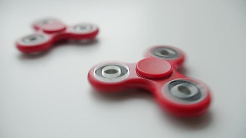 Close up of two red toy fidget spinners rotating over white background.