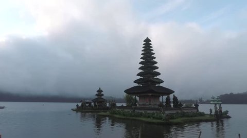Beautiful landscape footage of Ulun Danu Bratan Temple with cloudy sky and a tree as a frame in Tabanan, Bali, Indonesia. 