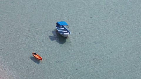 An orange kayak and a boat tied up in the shallow waters of the ocean beach drifting in the wind.