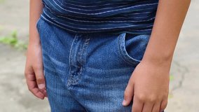 Closeup view of white child putting hands into pockets of blue denim jeans. Kid standing alone outside at pavement background. Real time full hd video footage.