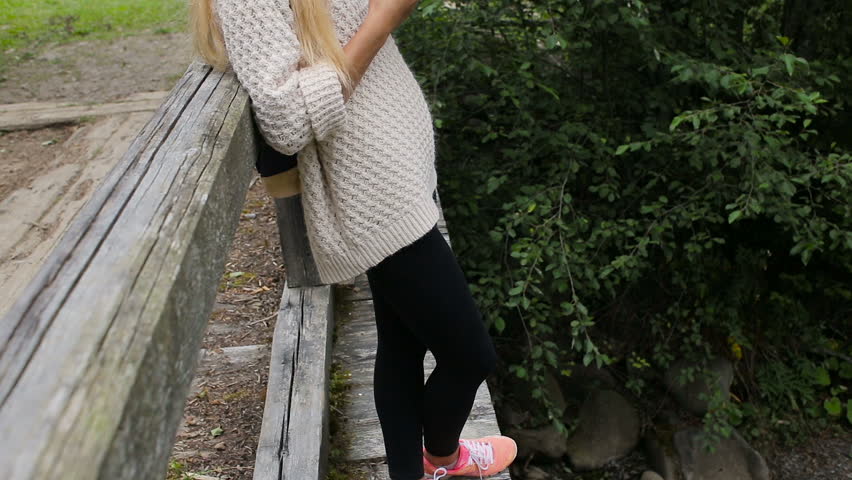 Young girl with a phone on a bridge over a mountain river