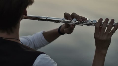 closeup of flutist playing in the sunset near water