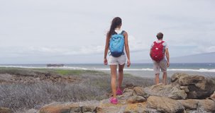 Young hiking couple walking on rocks at Shipwreck beach. Multiethnic male and female hikers are carrying backpacks. They are on summer vacation at Lanai, Hawaii. RED EPIC SLOW MOTION.