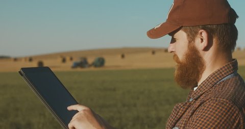 Modern farming concept, advanced technology in agriculture. Male farmer with portable tablet computer in a field using specialized app. 4K UHD 60 FPS