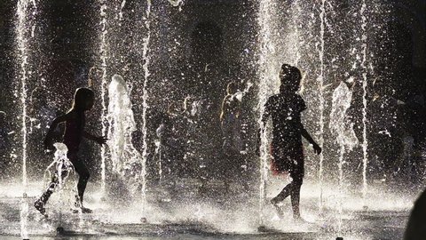 Children's silhouettes playing in the city fountain in slow motion on a summer day