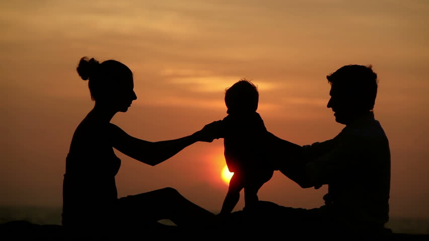 Silhouette of parents and small girl together over sunset