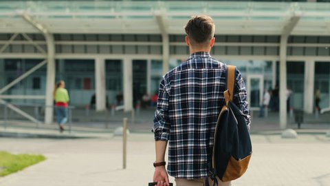 Young man walking to the modern airport terminal for his flight. View from the back.