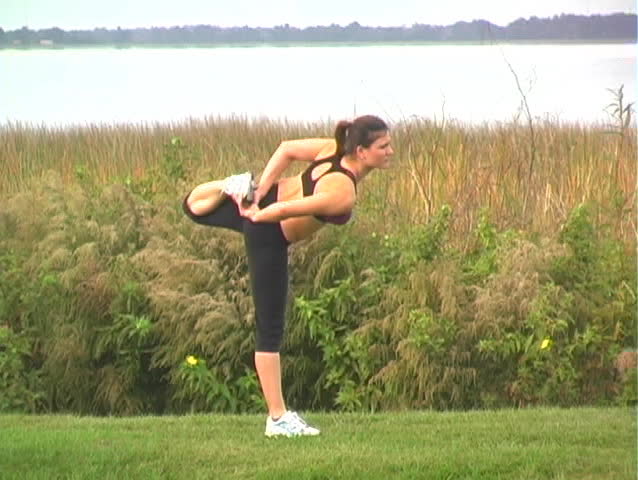 A lovely young brunette in a scenic municipal lakeside park, with remarkable muscle tone and wearing athletic apparel, stretches in preparation for a morning jog.