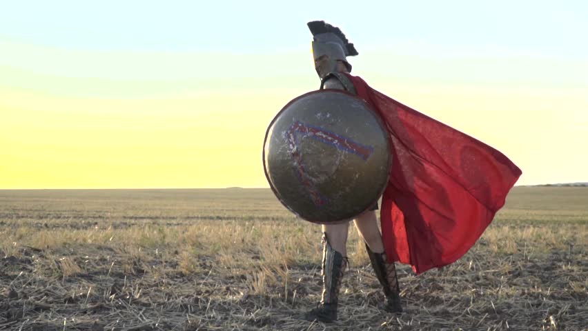 The majestic Roman legionary with a shield in his hand is standing in the field while in the wind his red cloak is blowing, slow motion Royalty-Free Stock Footage #29745520