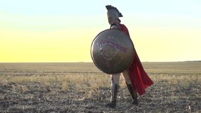 The majestic Roman legionary with a shield in his hand is standing in the field while in the wind his red cloak is blowing, slow motion - Powered by Shutterstock - Get 15% off with code: PIKWIZARD15