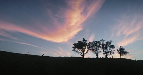 Aerial Silhouette of people walking on a Mt Eden volcano ridge at stunning epic sunset. The clouds are whispy and the trees are pohutukawa. Auckland, New Zealand
