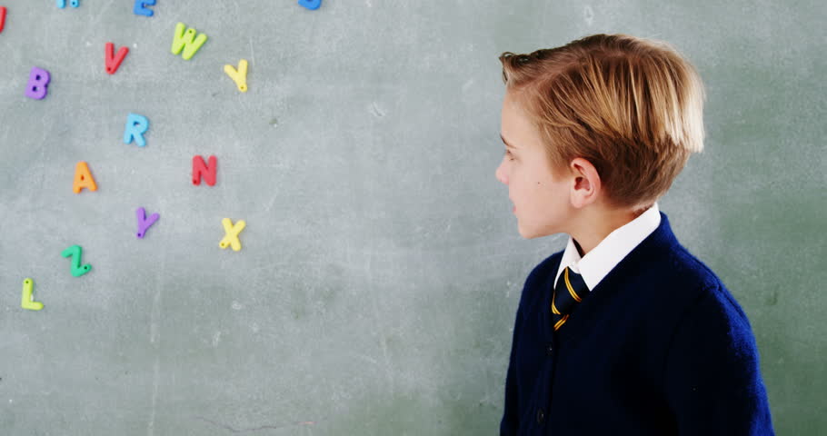 Rear view of Caucasian boy sticking alphabet b on chalkboard in classroom