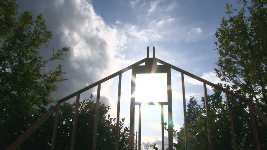 Camera tilt down revealing clouds and sun shining through window on framework of