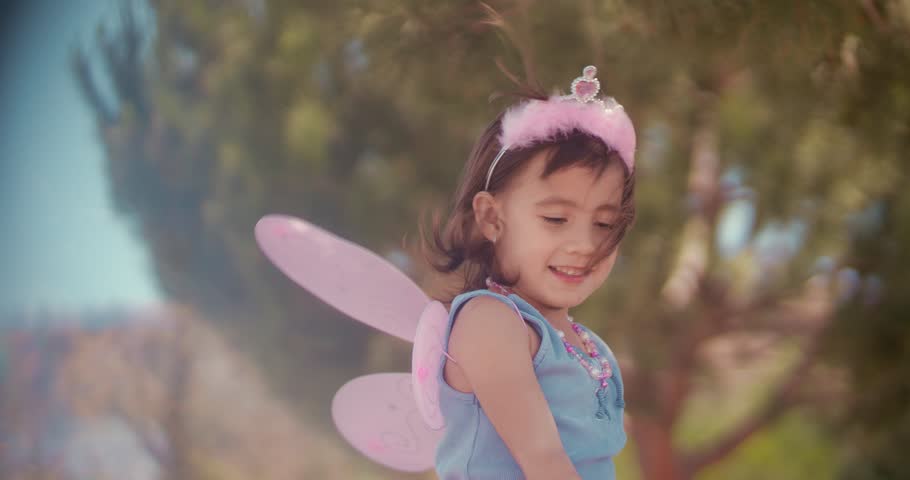 Happy little Asian girl dressed up in fairy queen costume playing with wand in park