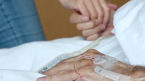 Woman holding husbands hand in a hospital bed with IV in his arms
