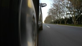 Driving a black sports / super car on a country road. Wheel spinning POV - Point of View, day country side, sunset, fall / winter. Trees on the side. Slow motion speed. Right side wheel / driving UK 