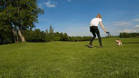 Young woman playing with dog Jack Russell terrier on the green meadow outside. Video footage