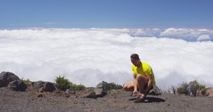 Runner athlete tying shoelaces going running on mountain above clouds. Young man is preparing to workout in nature on sunny day. RED EPIC SLOW MOTION.